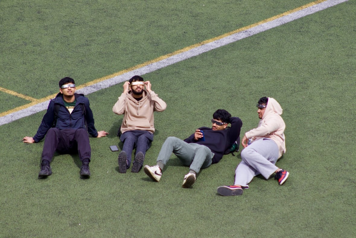 Four people in eclipse glasses lounge on a field
