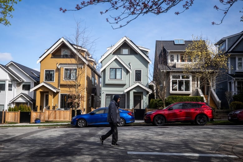 A man in a hooded sweatshirt walks past a row of colourful houses