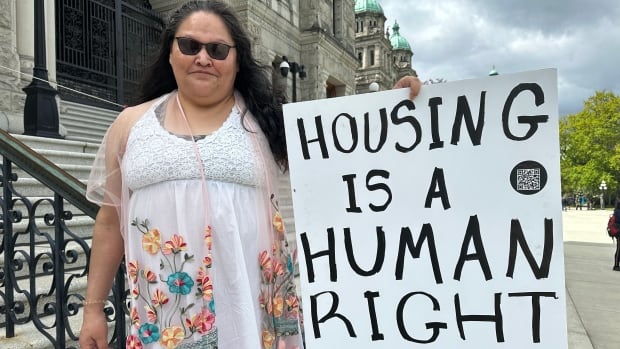 An Indigenous woman holds a sign that reads "Housing is a Human Right." 