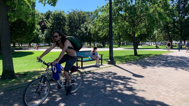 A shirtless man cycles through a park in Kelowna in 2022