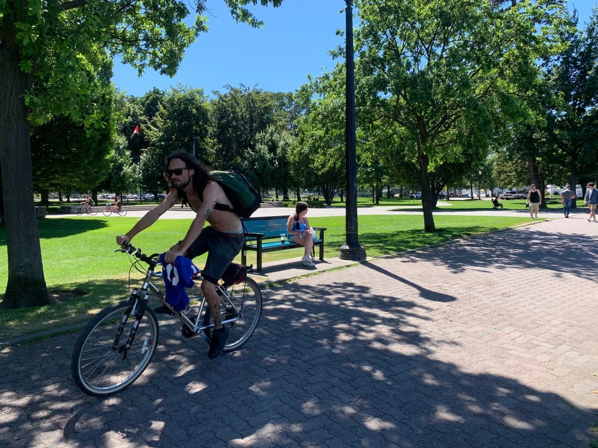 A shirtless man cycles through a park in Kelowna in 2022