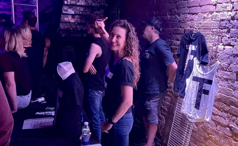 A woman stands behind a table smiling. On the wall behind her, there is a Full Throttle t-shirt and tank top.