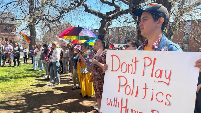 A person with short hair holds a sign reading "don't play politics with human rights."