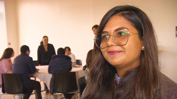 People from islands around the world sharing their knowledge at P.E.I. summit; Woman with glasses standing beside people at a table\.