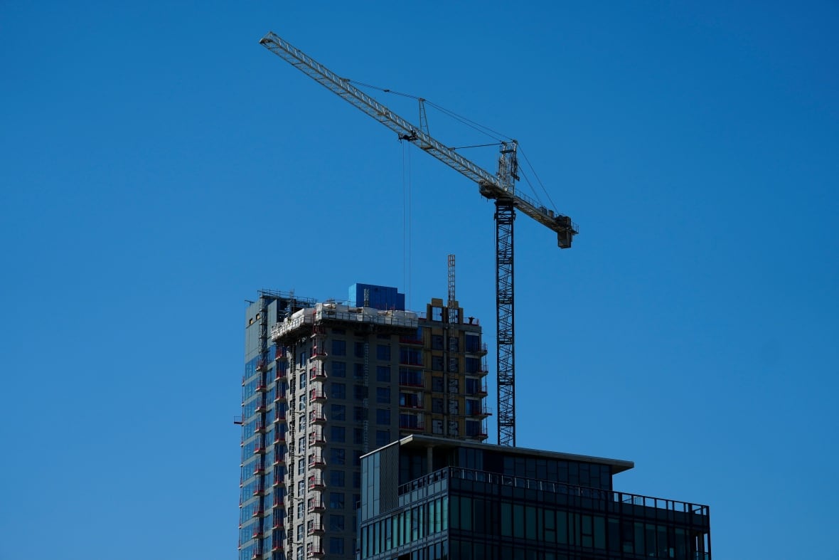 A highrise building under construction against a blue sky. There's a crane next to the building.