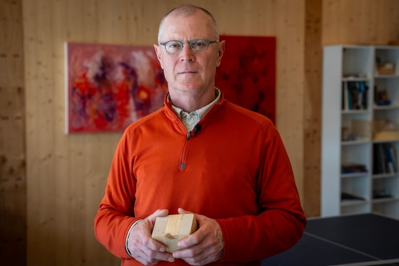 A man wearing blue-framed eyeglasses and an orange sweater is pictured inside a mass timber office building.