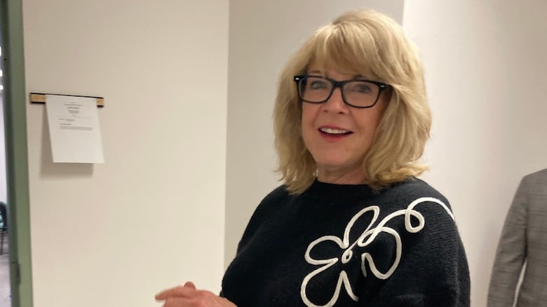 Woman with shoulder-length blond hair and black-rimmed glasses smiles at the camera.