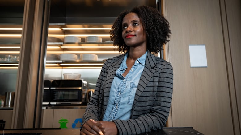 A woman in a blue shirt and grey-striped blazer poses in front of a shelf of plates. 