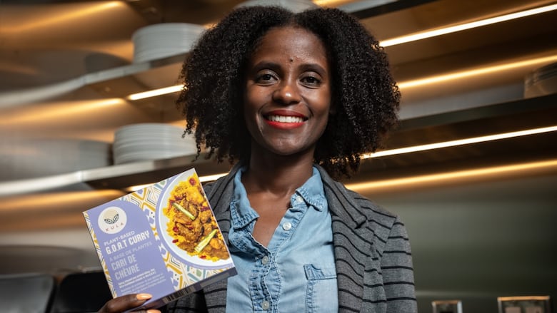A woman smiles while holding a purple package of plant-based curry.