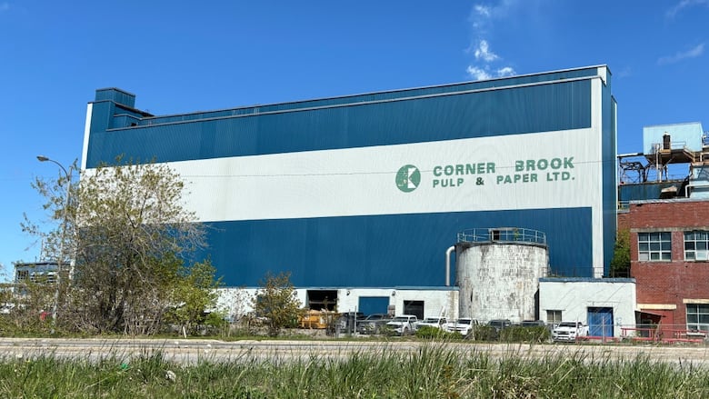 A blue industrial building with a company logo is pictured under a blue sky.