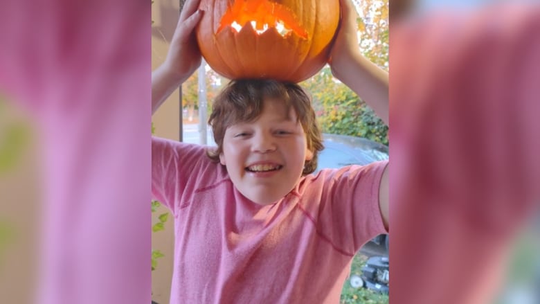 A boy holds a carved jack-o-lantern above his head.