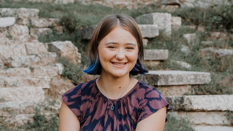 A portrait of a teenage girl with brown hair with blue highlights smiling into the camera.