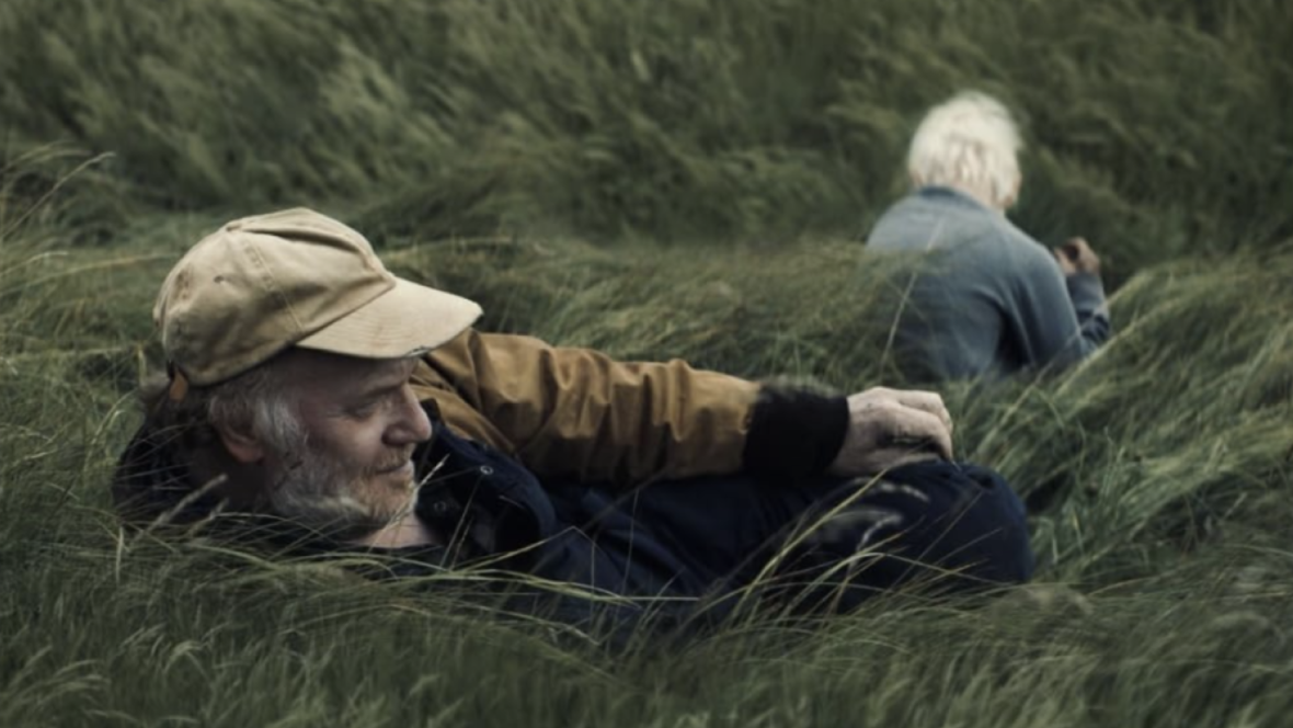 movie still of two older white men sitting in tall grass.