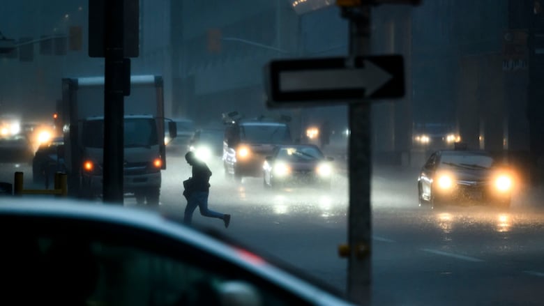 A busy intersection in the rain. One person runs across, holding a bag.