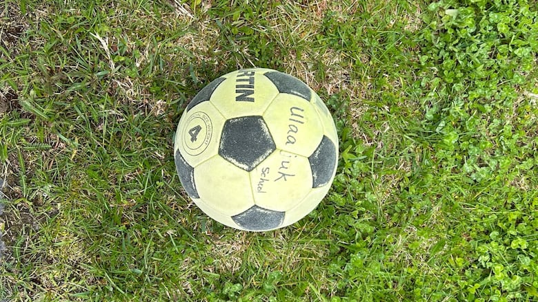 A faded soccer ball sitting on grass with the word "Ulaajuk" written on it in back marker.