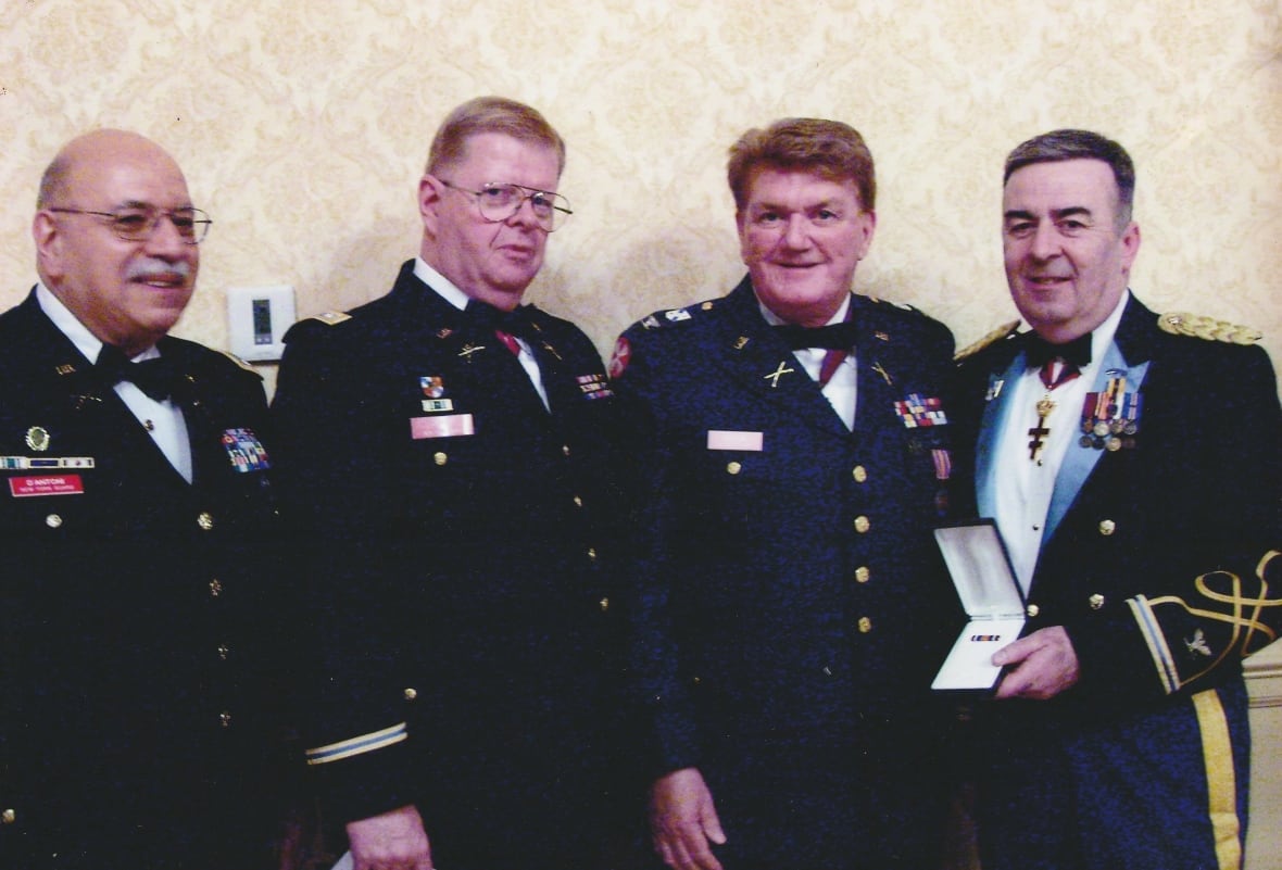 Four men in uniforms, one holding a medal in an open jewelry box.