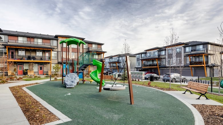 A playground with a tire swing and slide in front of townhouses.