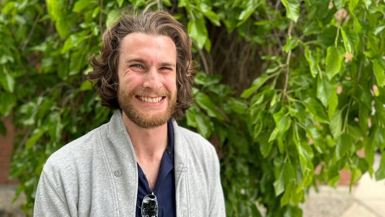 A man in his 20s grins at the camera. A tree is behind him. Brennan Willert thinks it's important to give blood, but is miffed Canadian Blood Services no longer does remote blood donor drives.