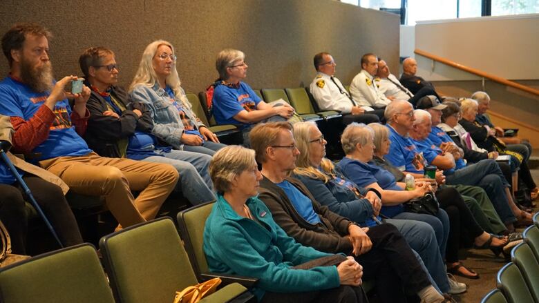 More than a dozen people sitting in chairs, they are all wearing a shirt that reads 'Beaver Lake is on fire.'