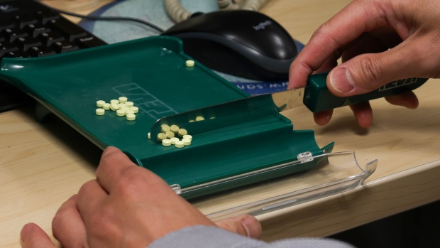 $4M worth of prescription opioids disappeared from an Ontario pharmacy. No one can say where they went; Hands move prescription medication in a tray near a mouse and landline phone\. 