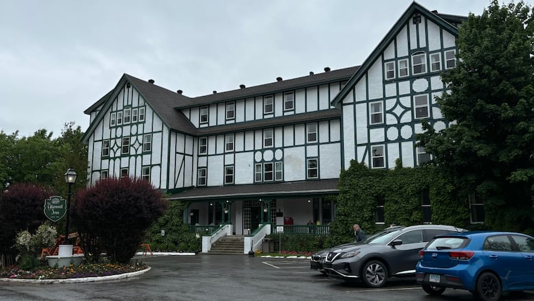 A large white and brown hotel sits behind trees with flowers around the front entrance.