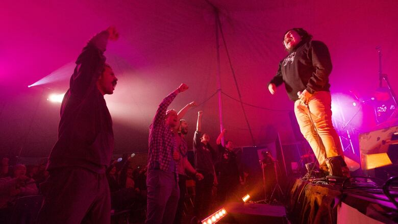 A performer screams on stage while audience members pump their fists 