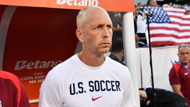 A men's soccer coach looks on.