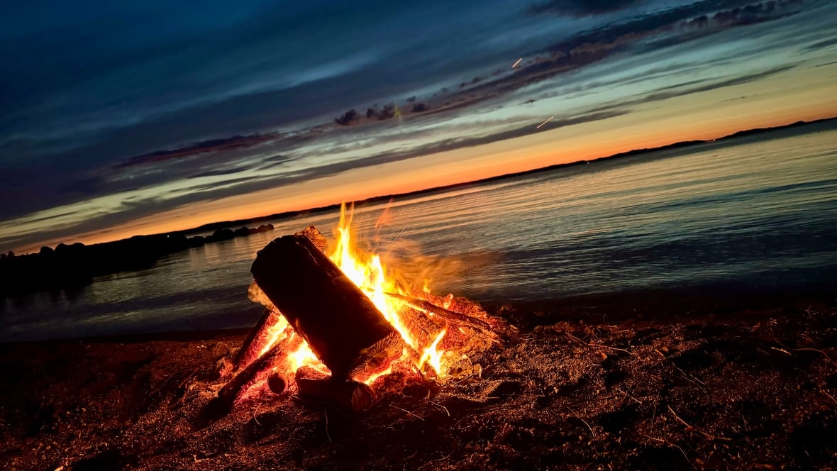 logs aflame on a beach as the sun sets over the ocean