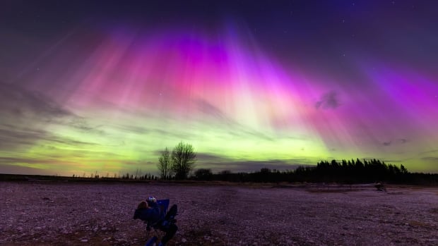 An onlooker gazes up at the spectacular northern lights display on May 10, 80 kilometres from Airdrie, Alta. There is a chance for more northern lights this week. A person lies in a chair in the foreground while the sky glows a spectacular purple, pink and green.