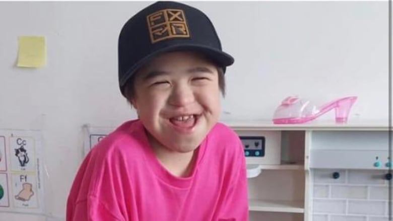 A boy wearing a pink shirt laughs and smiles at the camera.