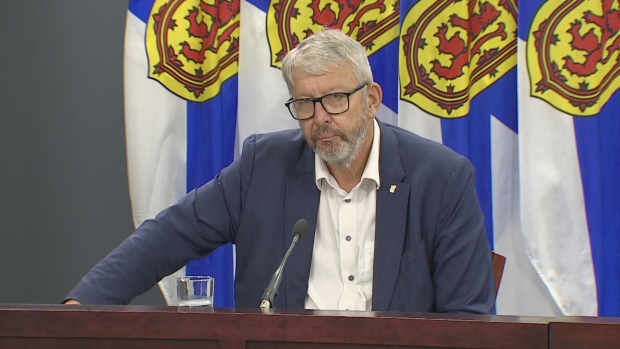 Province amending Halifax's charter to 'remove barriers' to housing development, minister says; man sits next to nova scotia flags\.