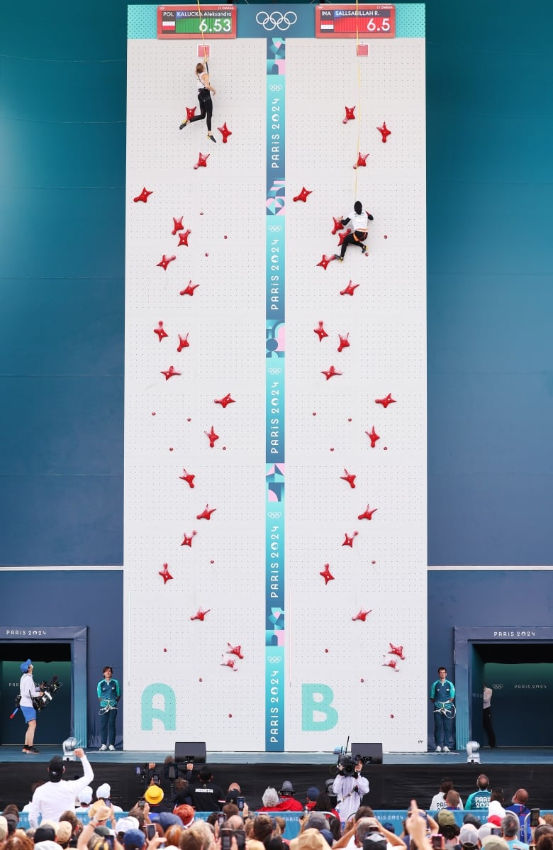 Climbers conquer a wall in front of the audience during a competition.