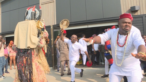 How the yam brings eastern Nigerians together in Fredericton; Performers surround the masquerade and fan him in attempts to calm his energy before entering the room\.  