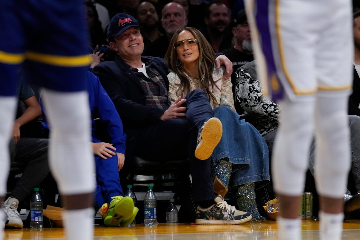 A couple watches a basketball game from the sidelines.