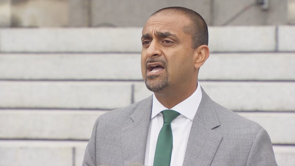 A man wearing a grey suit with a green tie standing outside behind grey steps. 