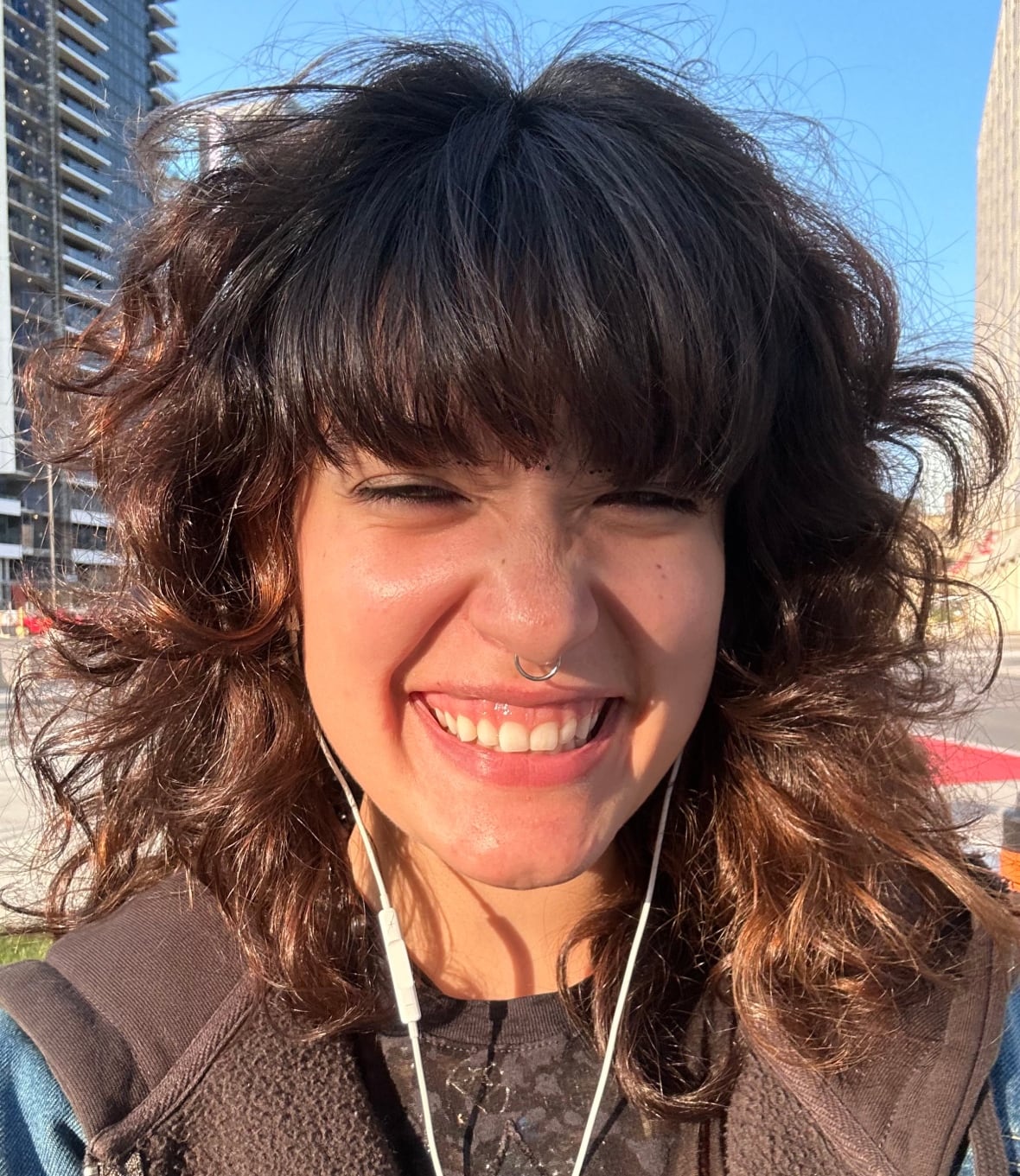 A woman wearing earbuds smiles at the camera. 