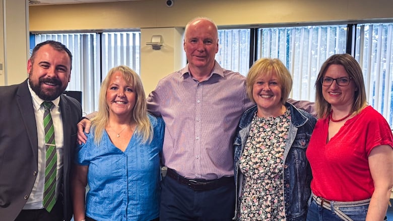 Five smiling people pose for a photo with their arms around each other