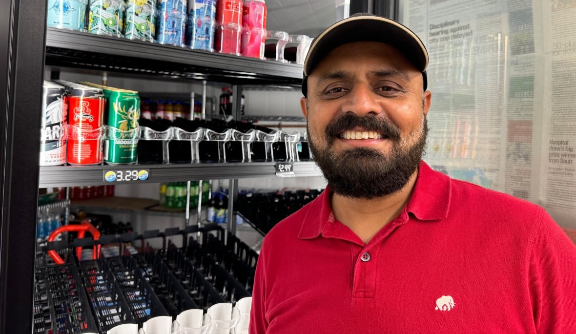 A smiling man wearing a hat stands in front of a beer cooler