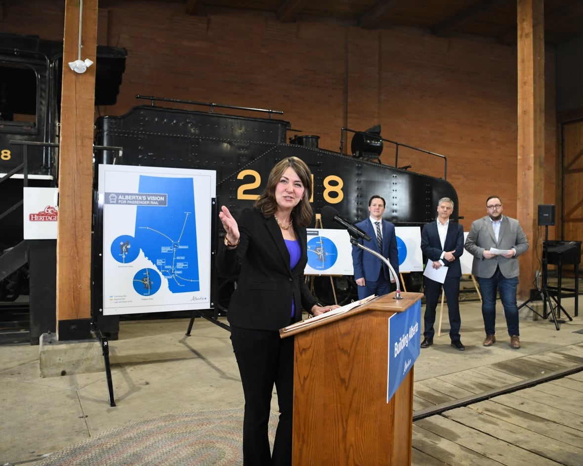 A woman points, standing in front of an old train and three men.