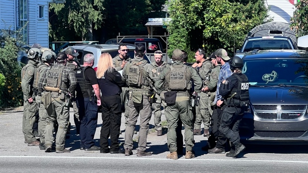 Terror suspect who entered Canada on student visa to await U.S. evidence in prison; A group of police officers in tactical gear stand in a circle at the side of a road\.