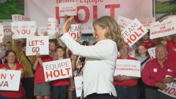 Leader Susan Holt says a Liberal government would start aiming for fiscal reform immediately if elected and says her party is aiming higher than a transfer of heavy industrial taxes to municipalities. A woman waves to the side of the room, with rows of adults and children wearing red in the background.