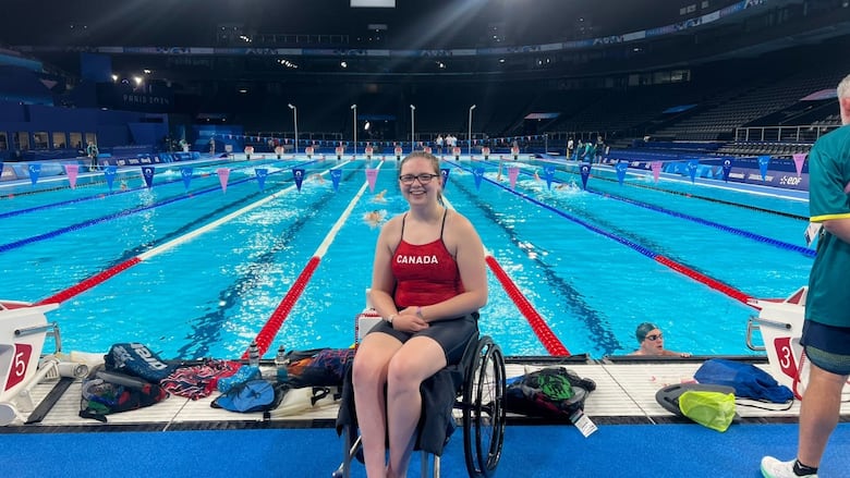 A woman in a team Canada bathing suit sits in her wheelchair in front of a pool.