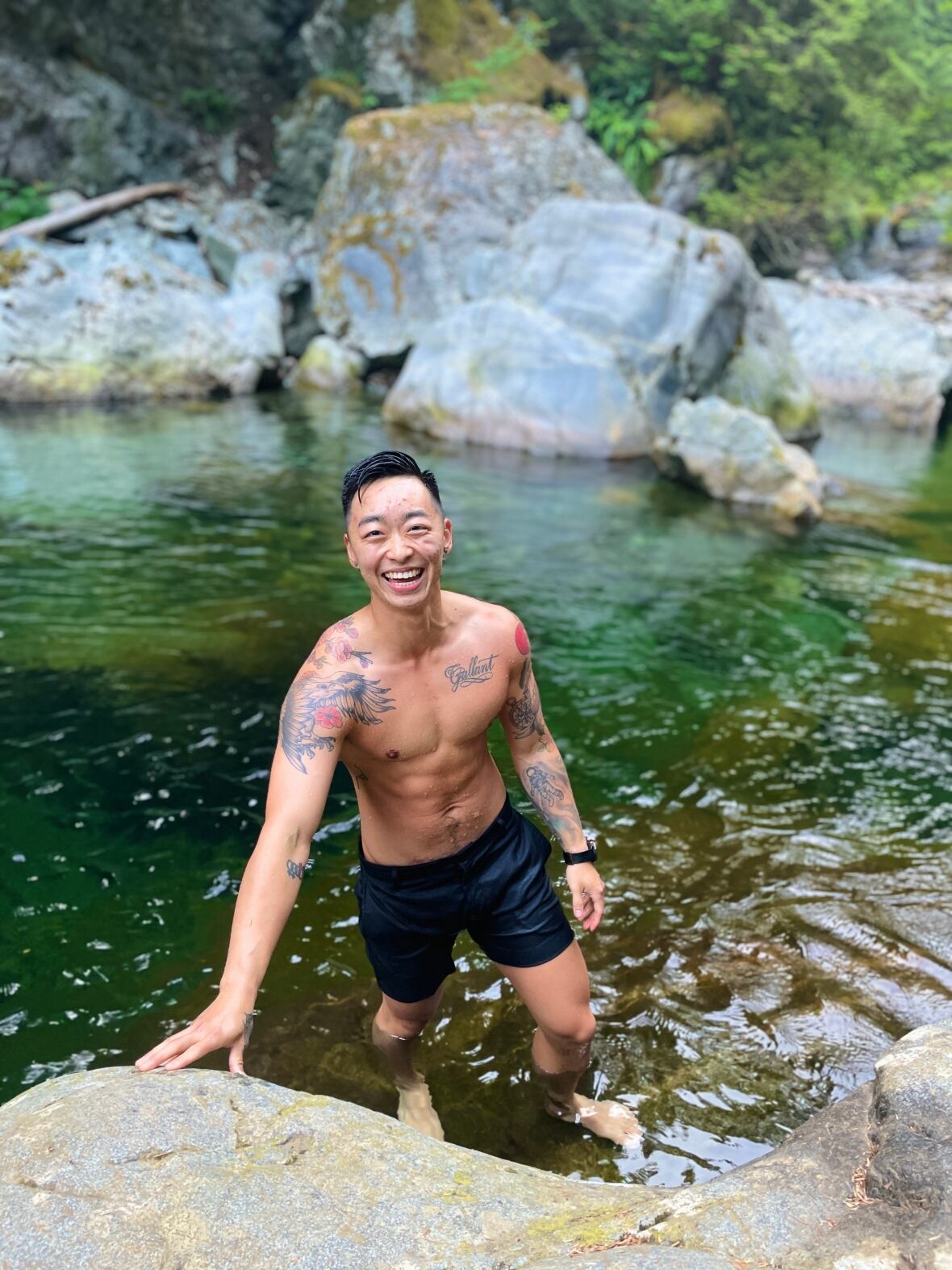 A man in a bathing suit smiles as he stands in a swimming hole. 