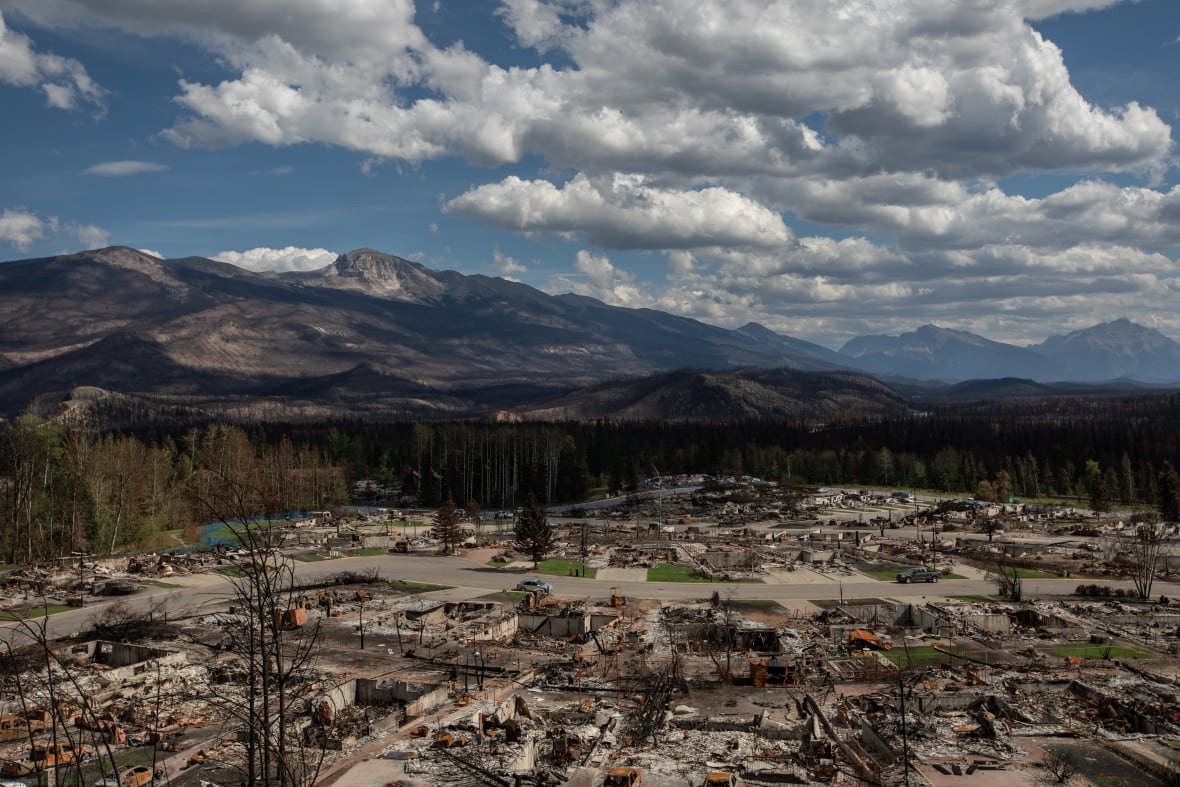 A view of a mountainous landscape. The wildfire-damaged townsite of Jasper is visible below.