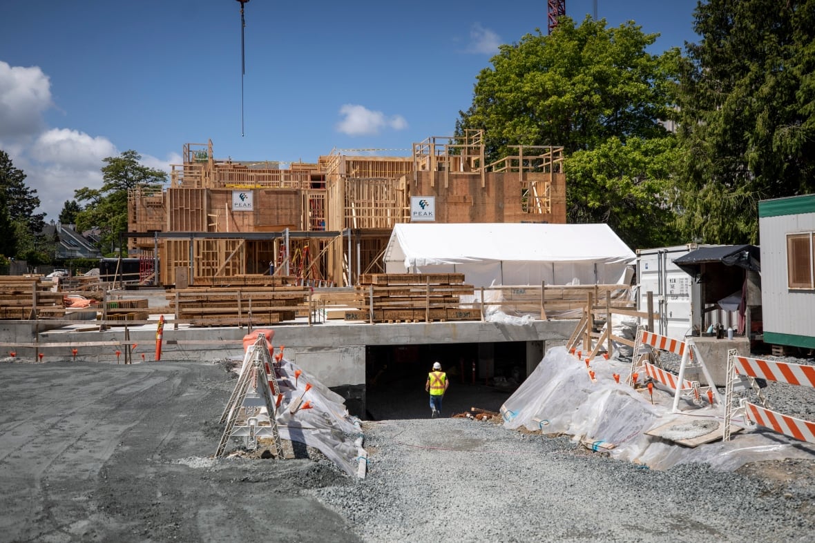 An under-construction home, with a worker in a high-vis vest entering an underground area.