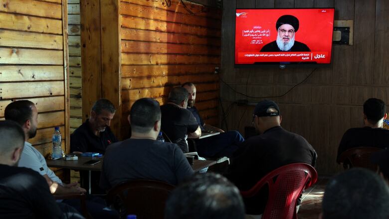 People sitting at a cafe as Nasrallah delivers televised address on the screen.