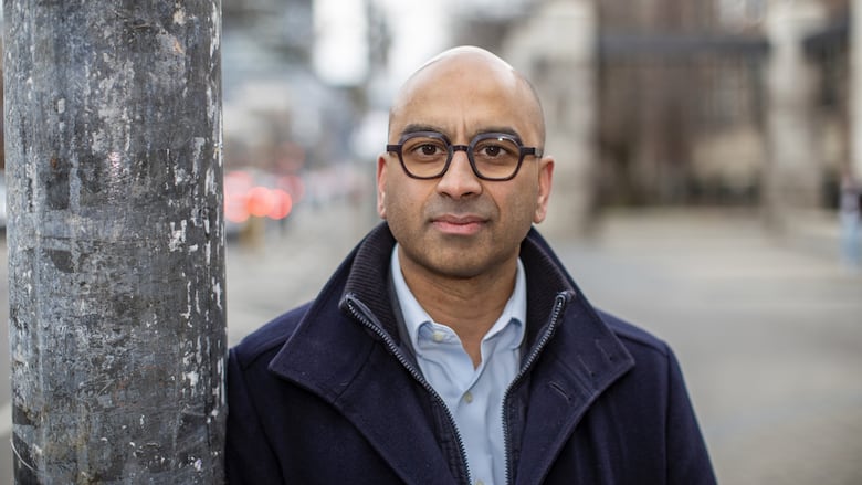 A bald Sri Lankan man with glasses looks at the camera