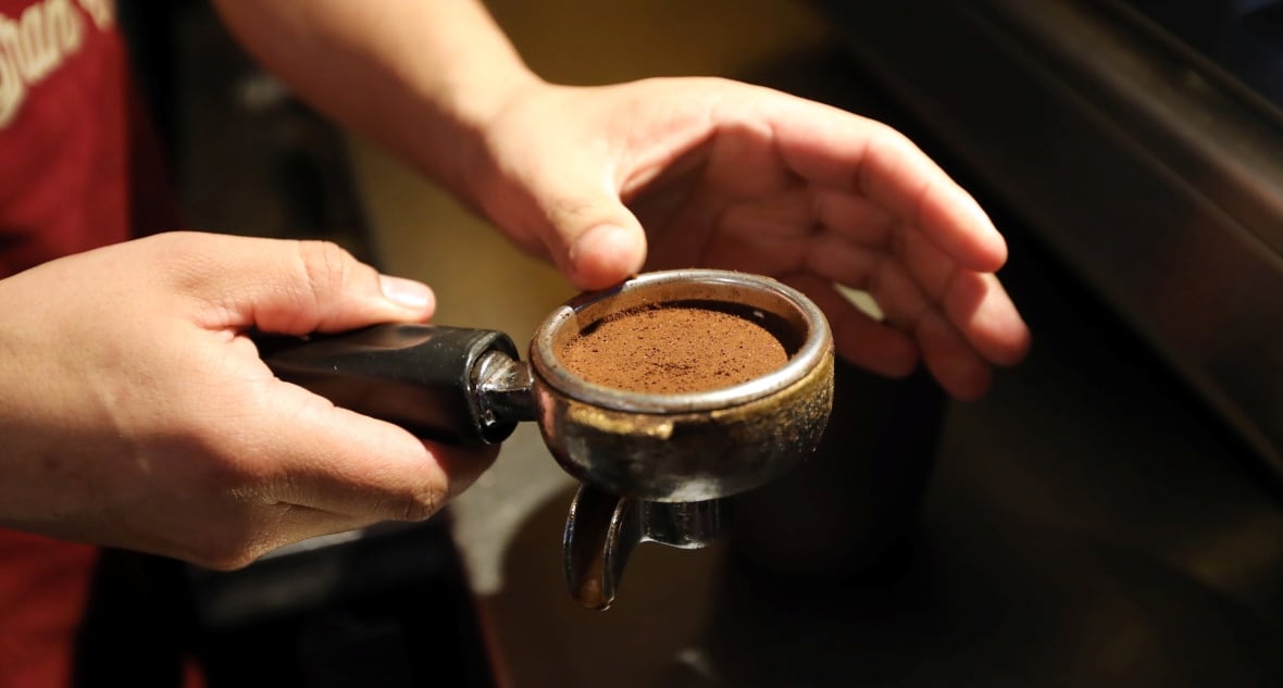 Close-up of a man holding an espresso machine cup full of espresso powder. 