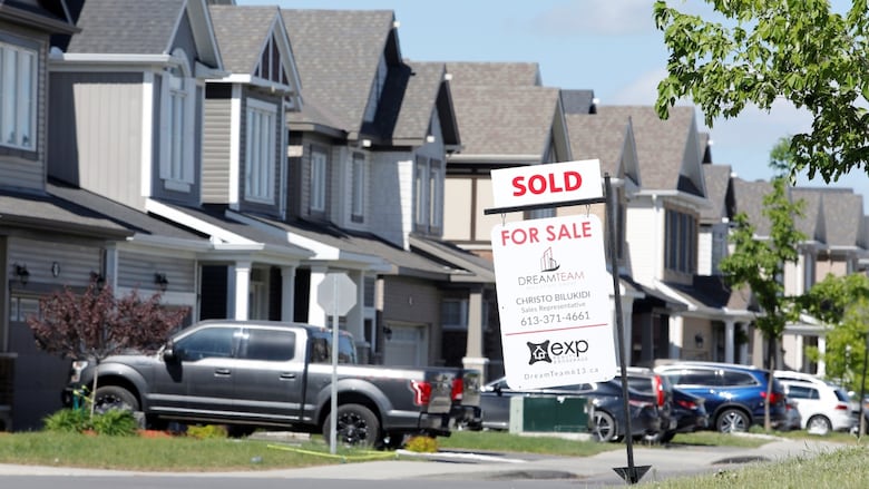 A realtor's for sale sign is seen standing outside a house.