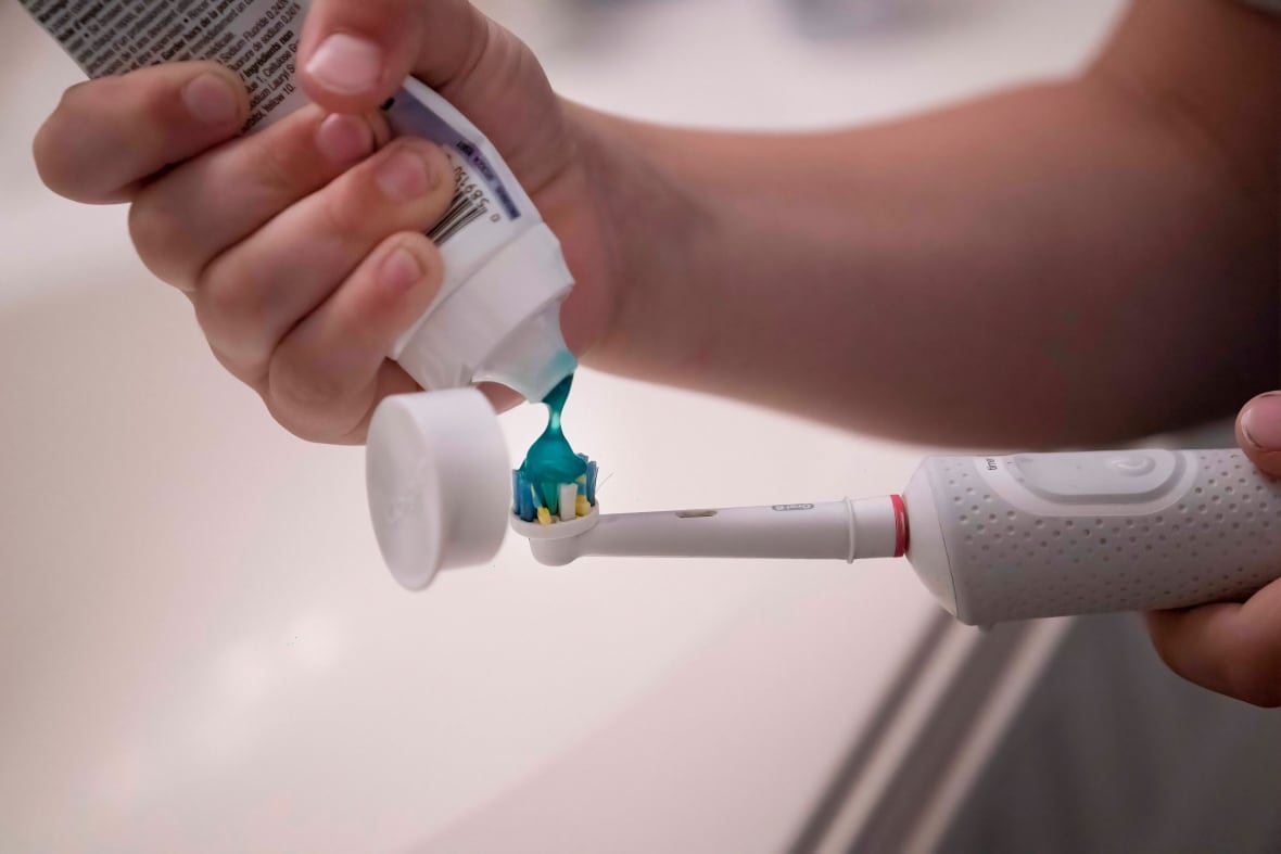 A child's hand puts toothpaste on a toothbrush.